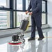 A man in a blue uniform using a Lavex single speed floor scrubber to clean a floor.