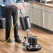 A man using a Lavex rotary floor machine with a yellow hose to clean the floor in a professional kitchen.