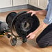 A person using a Lavex single speed rotary floor machine with a black circular brush to clean a floor.