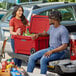 A man and woman sitting on the back of a truck with a red CaterGator cooler.