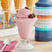 A glass of pink ice cream with cherries and a spoon next to a bottle of LorAnn Black Cherry Flavor Fountain syrup.
