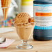 A bowl of ice cream with a scoop and LorAnn Butterscotch syrup in a glass on a counter.