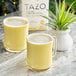 A glass mug of Tazo Turmeric Latte next to a plant on a marble table.