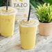 A plastic cup of Tazo Turmeric Latte with a yellow straw next to another cup of Tazo Turmeric Latte with a yellow straw.