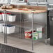 A Regency metal shelf with a wooden top on a stainless steel counter.