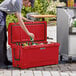 A man placing a bottle of beer in a red CaterGator outdoor cooler.