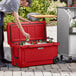 A man opening a red CaterGator outdoor cooler and putting a can inside.