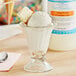 A glass cup with a scoop of New York cheesecake flavored ice cream and a spoon in it.