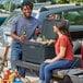 A man and woman sitting on the back of a truck with a CaterGator outdoor cooler.