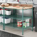 A Regency green metal shelving unit with wooden shelves on a white counter.