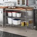 A Regency stainless steel kitchen shelf with a wooden insert on a metal shelf with food containers.