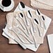 A group of Acopa stainless steel demitasse spoons on a table with a cup of coffee and a napkin.