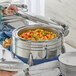 A woman using an Acopa Manchester chafer to serve food from a buffet table.