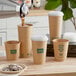 A person pouring coffee into a New Roots brown paper cup with a green logo.