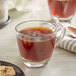 A glass cup of brown Crown Beverages Organic French Roast coffee with a spoon and cookies on a table.