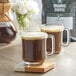 Two glass mugs of Crown Beverages Organic French Roast Whole Bean Coffee on a wooden tray.