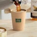 A hand pouring coffee into a New Roots Double Wall Kraft paper hot cup.