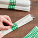 A person wrapping a napkin with green and white checkered paper.