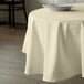 An ivory table with a white Intedge round tablecloth and a white plate on it.