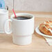 A Tuxton eggshell china mug filled with coffee with a straw and a pastry on a table.