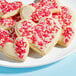 A heart shaped cookie with white frosting and pink Adourne Valentine's Day sprinkles.