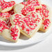 A plate of heart-shaped sugar cookies decorated with white icing and red, pink, and white sprinkles.