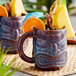 Two Libbey brown tiki mugs filled with fruit slices.