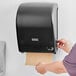 A person using a Lavex Translucent Black paper towel dispenser.