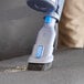 A person using the blue Lavex stick vacuum with a brush to clean a chair.