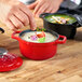 A person using a Chasseur ruby red enameled cast iron pot to prepare food.