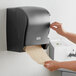 A person using a Lavex black lever activated paper towel dispenser.
