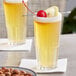 A pair of Duralex highball glasses filled with yellow liquid and cherries.