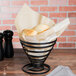 A black metal basket with Bagcraft Packaging EcoCraft cone liners inside on a bakery counter.