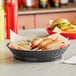 A black Tablecraft diner platter basket with hot dogs and fries in it.