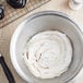 A bowl of white frosting with a whisk next to a white container of LorAnn Oils White Liquid Gel Food Coloring.