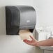 A hand reaching out to a Lavex translucent black automatic paper towel dispenser.