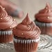 A chocolate cupcake with brown frosting on a wire rack.