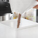A person pouring UPOURIA Salted Caramel Hot Chocolate mix into a container.