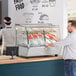 A man standing at a counter with food in a ServIt countertop heated display case.