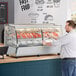 A man standing at a counter with food in a ServIt countertop heated display case.