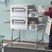 A man in a white apron and hat standing in front of a Lincoln Impinger II double conveyor oven.