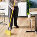 A man using a Lavex yellow fiberglass broom handle to sweep the floor in a corporate office cafeteria.