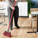 A person using a Lavex 48" red metal broom handle to sweep the floor in a corporate office cafeteria.