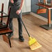 A person sweeping the floor with a Choice Economy Angled Broom.