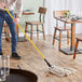 A person holding a Lavex yellow fiberglass mop handle with a metal jaw style attachment mopping a wooden floor.