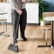 A man using a Lavex black fiberglass broom handle to sweep the floor in a professional kitchen.