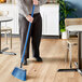 A person using a Lavex blue fiberglass broom handle to sweep the floor in a corporate office cafeteria.