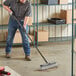 A man using a Lavex black threaded fiberglass broom handle to sweep the floor.