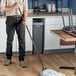 A man using a Lavex Black metal mop handle to mop the floor in a professional kitchen.