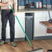 A man using a Lavex metal rod with a black handle to sweep the floor.